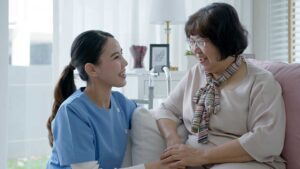 A senior resident sitting in a sunny lounge with a small dog on their lap and a window view of a garden outside.